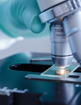 Close up view of scientist hands with gloves set the sample in the microscope for research