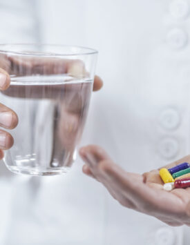 Doctor`s hand holding colorful pills and glass of water